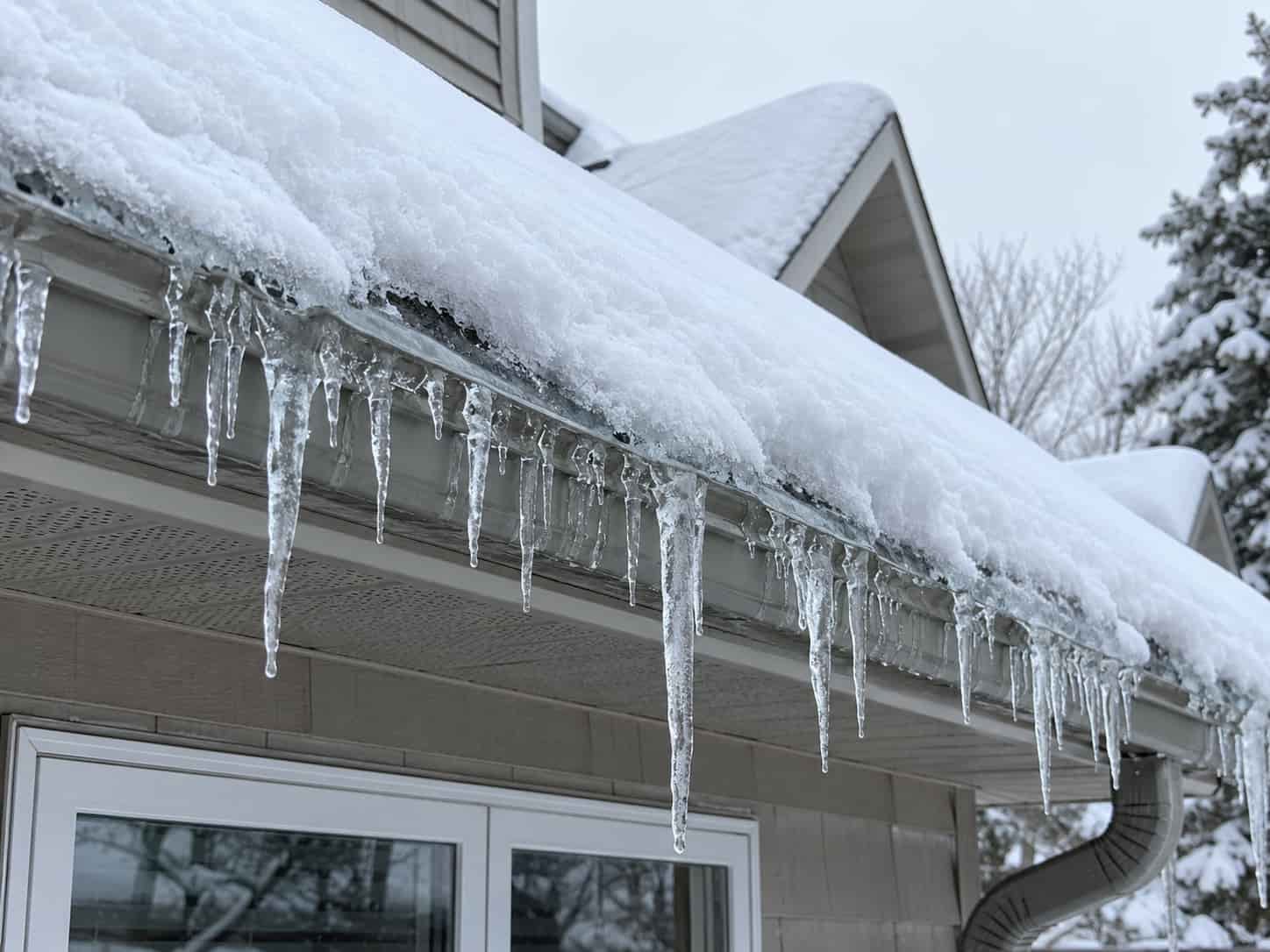 Snow-covered residential roofline with icicles forming along the eavestrough edge
